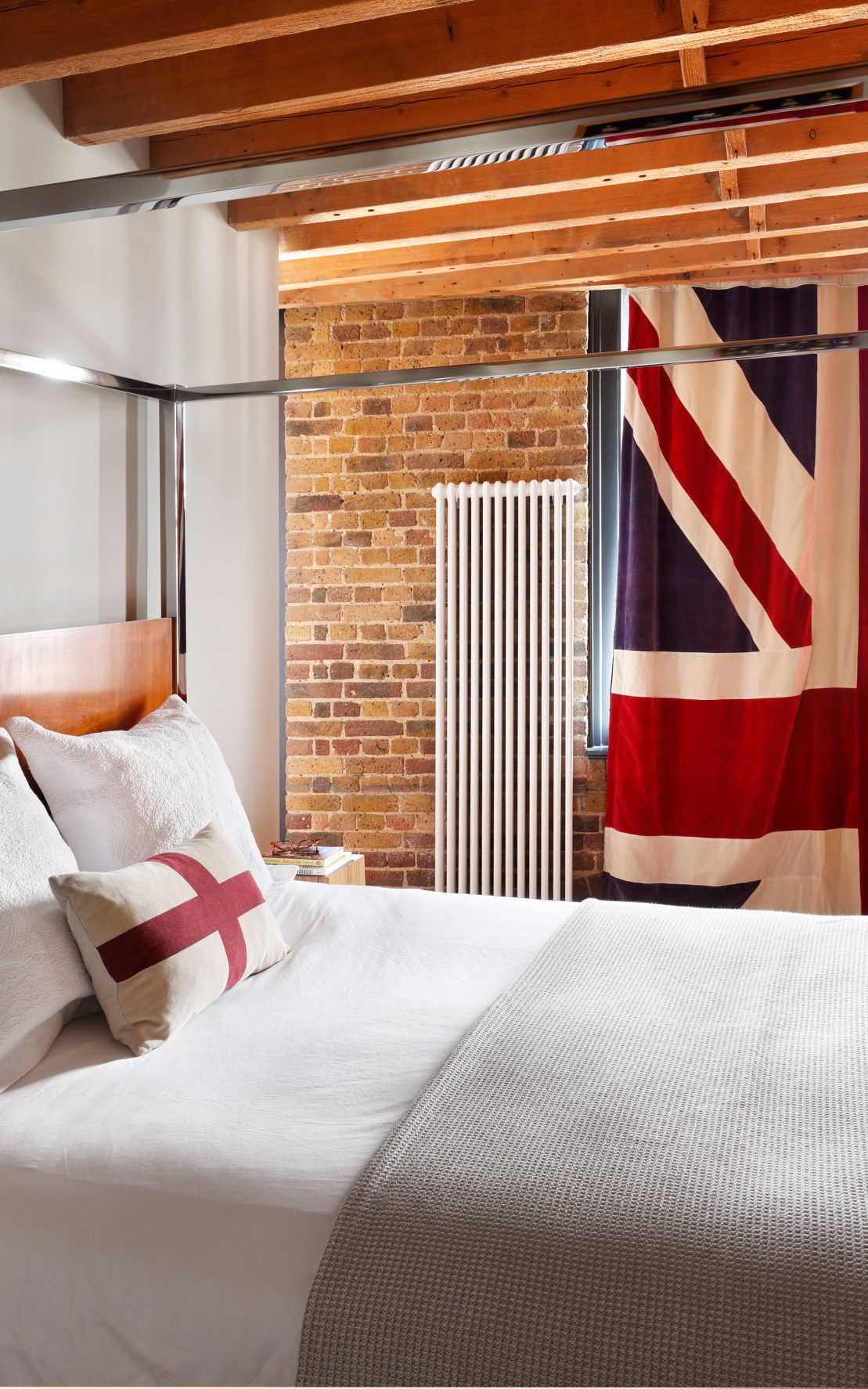 Modern loft bedroom of Tom Daley with elevated bed and partial view of THE LINE bar stool used as a side table.