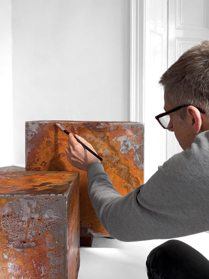Tomasz Danielec hand-painting rust finish onto THE BOX table inside a palace setting, emphasizing artisanal process and luxury environment.